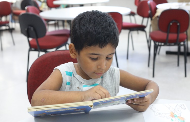 criança sentada em uma mesa lendo um livro 